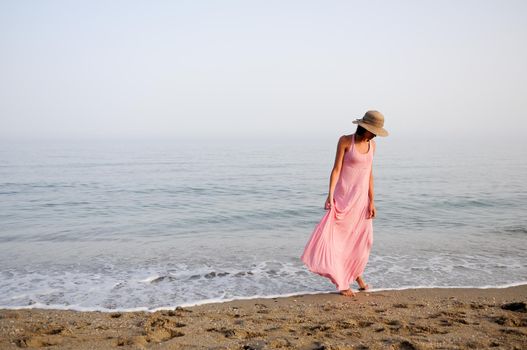 Portrait of a beautiful woman with long pink dress and sun hat on a tropical beach