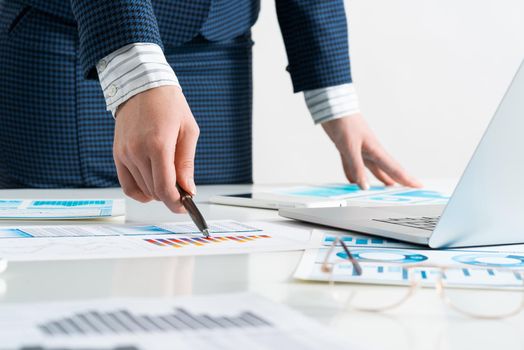 Businesswoman standing near office desk with laptop and documents. Financial audit and consulting. Corporate manager in suit working with online business analytics. Investment and stock trading
