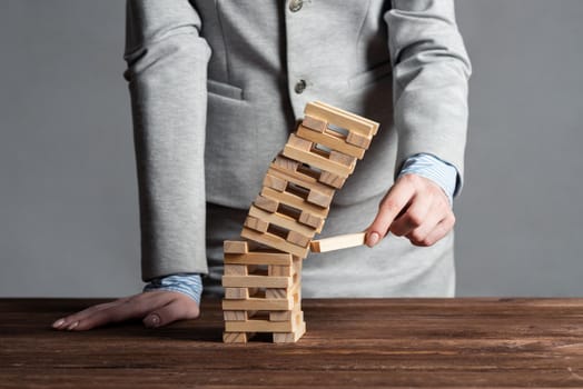Businesswoman removing wooden block from falling tower on table. Management of risks and economic instability concept with wooden cubes game. Failure and collapse in corporate business