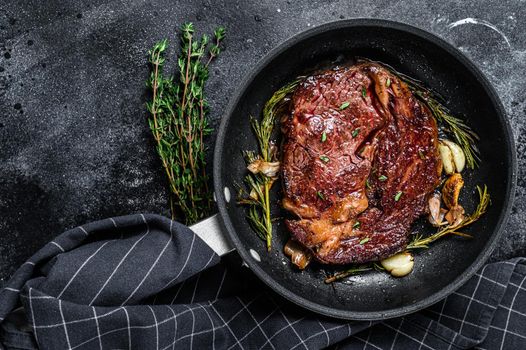 Roasted rib eye steak, ribeye beef meat in a pan. Black background. Top view. Copy space.