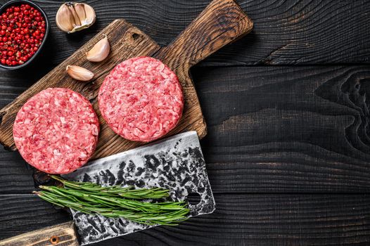 Raw steak cutlets with mince beef meat and rosemary on a wooden cutting board with meat cleaver. Black Wooden background. Top view. Copy space.