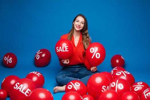 caucasian woman with attractive appearance sits with baloons with percent print, picture isolated on blue background