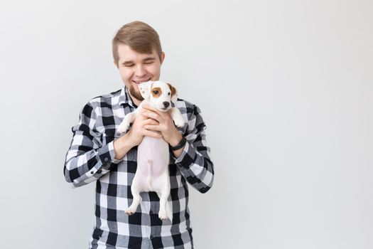 people, pets and animals concept - young man holding jack russell terrier puppy on white background.