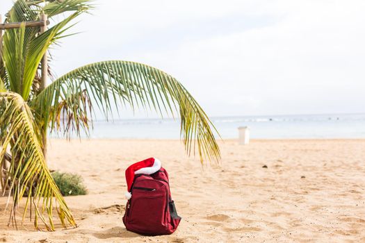 Santa Claus hat on backpack standing on sand beach. Christmas and New Year celebration. Nobody.