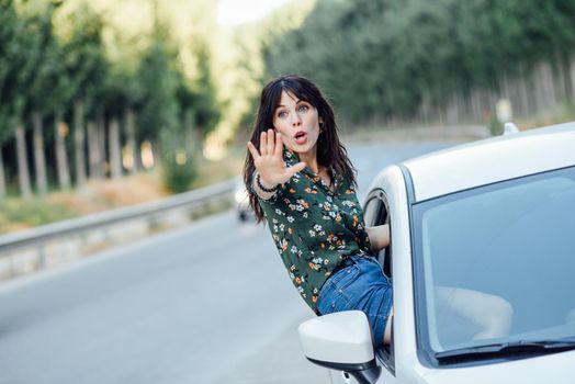 Young funny woman peeking her body through the window of the car in a beautiful poplar field. Lifestyle concept.