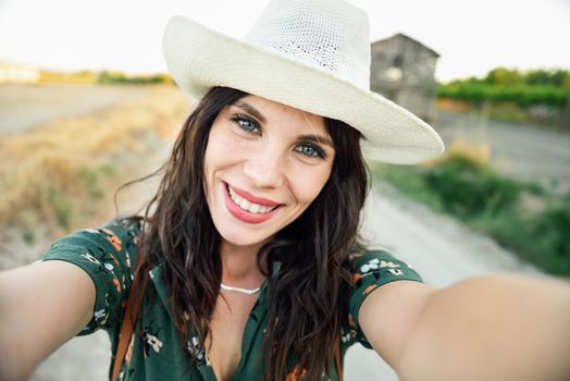 Beautiful hiker young woman, wearing flowered shirt, taking a selfie photograph outdoors