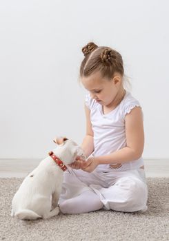 Childhood, pets and dogs concept - Little puppy and child girl in white shirt having fun.