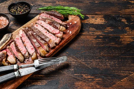 Ribeye steak on the bone. Grilled Beef meat. Wooden dark background. Top view. Copy space.
