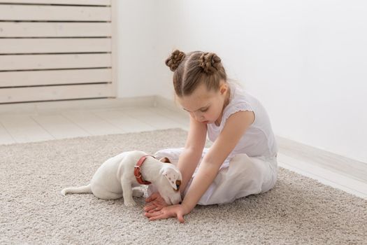 people, children and pets concept - little child girl lying on the floor with cute puppy and playing.