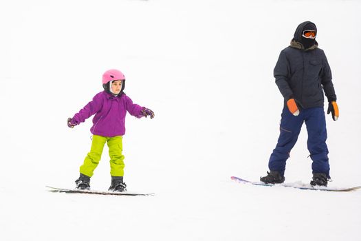 Instructors teach a child on a snow slope to snowboard