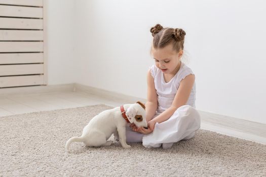 Children, pets and animals concept - little child girl in pajamas playing with puppy on the floor.