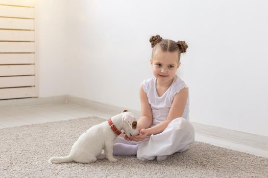 Children, pets and animals concept - little child girl in pajamas playing with puppy on the floor.