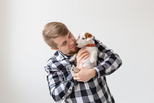 people, pets and animals concept - handsome man holding jack russell terrier puppy on white background.