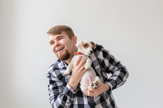 people, pets and animals concept - handsome man holding jack russell terrier puppy on white background.