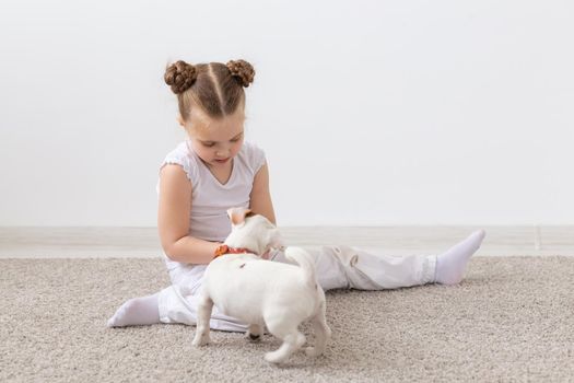 Childhood, pets and dogs concept - Little puppy and child girl in white shirt having fun.