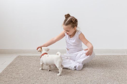 Dogs, pets and children concept - little child girl playing on the floor with cute puppy.
