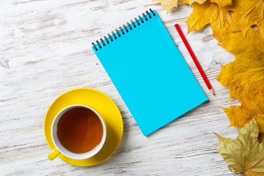 Flat lay autumn composition with cup of black tea and yellow autumn leaves. Time of tea break concept. Still life of hot drink and notepad with pen lies on vintage wooden desk with bright foliage.