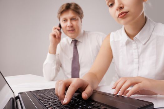 Coworkers working with a laptop and a cellphone in an office, the laptop is at the front