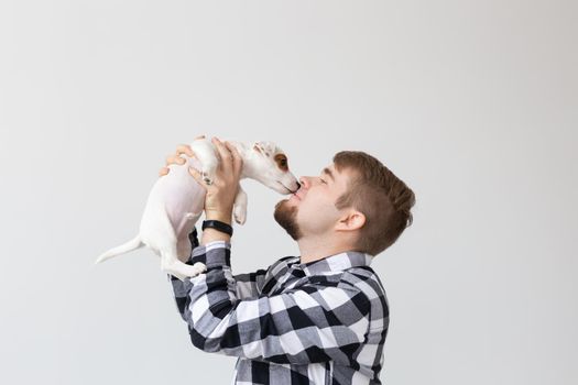 people, pets and animals concept - young man kissing jack russell terrier puppy on white background.