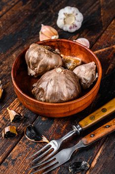 Bulbs and cloves of fermented black garlic in a plate. Dark wooden background. Top view.