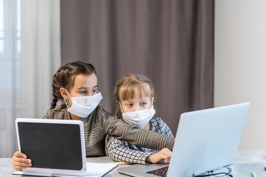 Distance Learning. School Girls At Laptop Wearing Mask Studying Online Sitting at the table at home