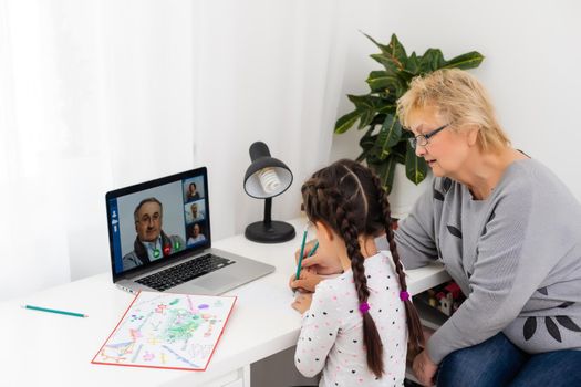 Cute and happy little girl child using laptop computer with her grandma, studying through online e-learning system.