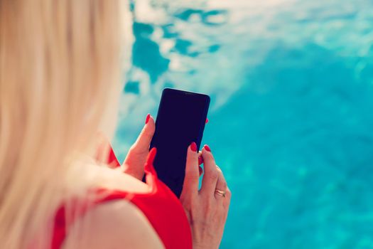 Woman hand using smartphone near swiming pool