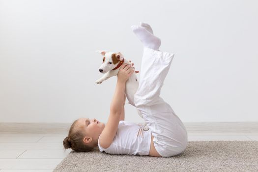 people, children and pets concept - little kid girl lying on the floor with cute puppy in hands.