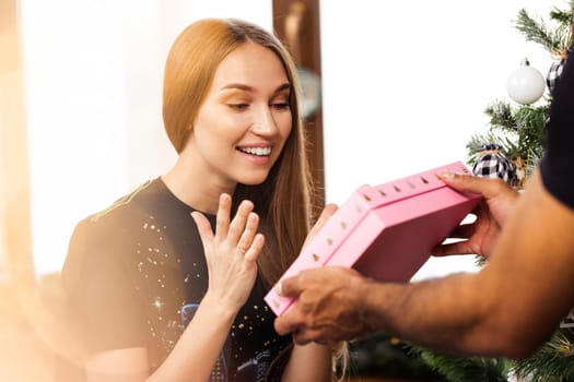 Surprised young woman opens a pink box with a present inside it