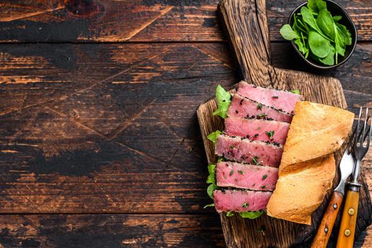 Grilled Ahi Tuna Steak and Avocado Sandwich with arugula on a cutting board. Dark wooden background. Top view. Copy space.