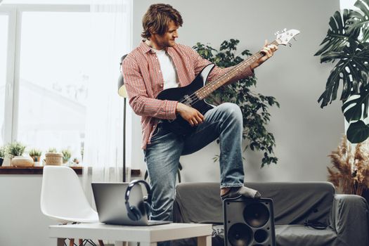 Man playing electric guitar and recording music into laptop at home