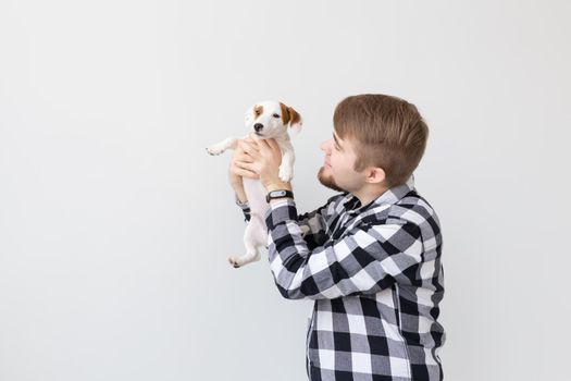 people, pets and animals concept - young man holding jack russell terrier puppy on white background with copy space.