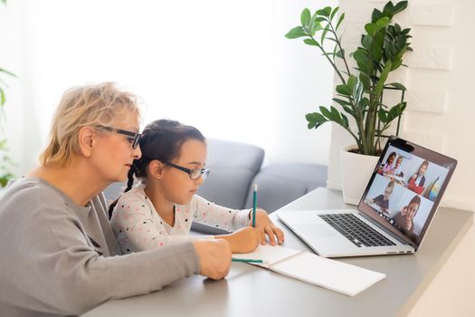 Cute and happy little girl child using laptop computer with her grandma, studying through online e-learning system.