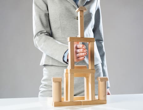 Business woman building tower on table from wooden blocks. Strategy planning and development concept. Young woman wearing formal wear sitting in office interior. Successful company building and growth