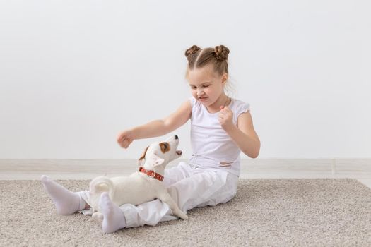 Children, pets and dogs concept - Child girl dressed in pajamas sitting on the floor and playing with puppy.