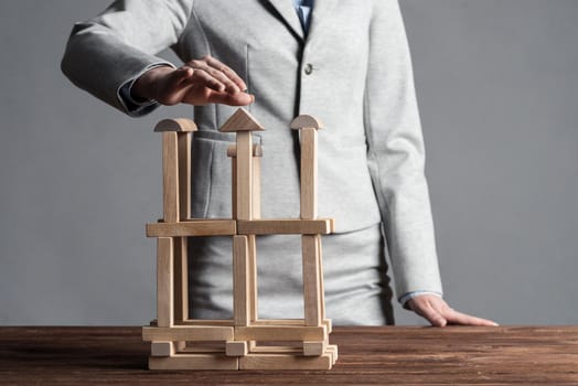 Business woman building tower on table from wooden blocks. Strategy planning and development concept. Young woman wearing formal wear sitting in office interior. Successful company building and growth