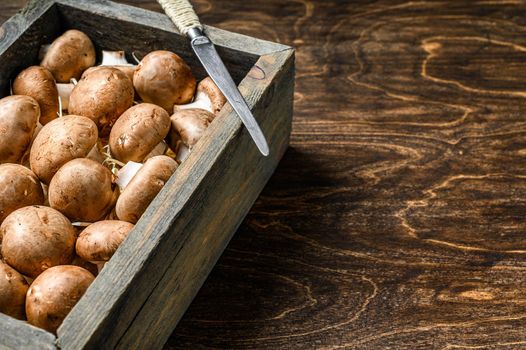 Raw Fresh champignon mushrooms in a wooden box. Dark background. Top view. Copy space.