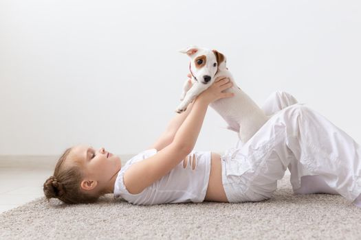 People, pets and animal concept - Little girl sitting on the floor over white background and holding puppy Jack Russell Terrier.