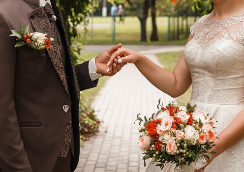 The groom in a brown suit holds the bride's hand with a wedding bouquet.