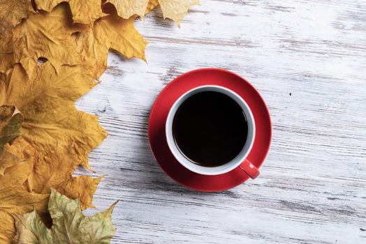 Flat lay autumn composition with cup of black tea and yellow autumn leaves. Time of tea break concept. Hot beverage lies on vintage wooden desk with bright foliage. Still life of morning tea ceremony.
