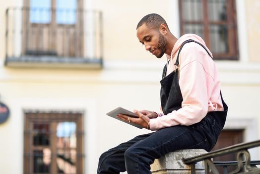 Young black man using digital tablet in urban background. Lifestyle and technology concepts.