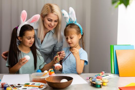 Young mother and her two little daughters painting colorful Easter eggs at home