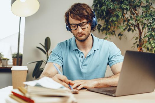 Young man in blue shirt sits at the table and studies with laptop close up