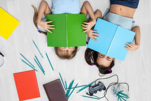 people, children, friends, literature and friendship concept - two happy girls lying on floor and reading book at home