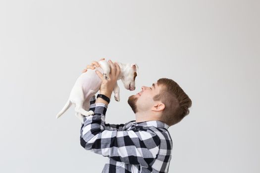 people, pets and animals concept - young man kissing jack russell terrier puppy on white background.