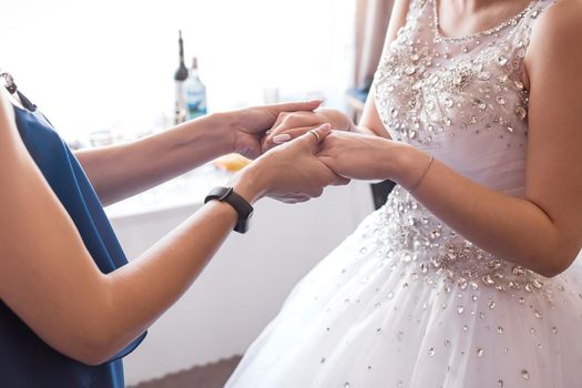 Mom and bride in white dress hold hands, close-up.