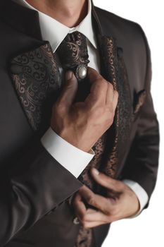 A man in a white shirt and brown luxury suit adjusts the tie with the pearl with his hands close-up.