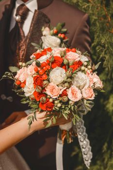The bride holds in her hand a wedding decorative bouquet of live flowers of red and white roses.