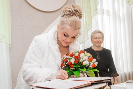 Attractive cute bride of European blonde appearance puts a signature about consenting marriage at the wedding. Belarus, Minsk region - January 23, 2021.