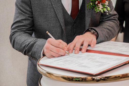 The groom's hands are signed with a pen in the document on the confirmation of the marriage close-up.
